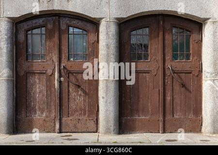 Une paire de portes doubles en bois rustiques avec des textures altérées et des accents de fer complexes, dans un cadre en pierre grise. Le design respire c historique Banque D'Images