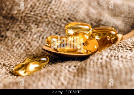 Capsules d'huile de poisson dans une cuillère en bois. Pilules d'huile de poisson, comprimés sur la toile de jute. Complexe vitaminique oméga 3,6,9. Capsules d'huile de poisson avec oméga-3, vitamine D. Banque D'Images