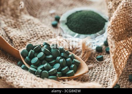 Cuillère en bois avec des comprimés de spiruline, poudre de chlorella sur fond de toile de jute. Superaliment détox Banque D'Images