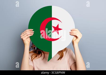 Algérie News concept. Mains féminines tenant une affiche d'information ronde avec drapeau Algérie isolé sur fond gris de studio Banque D'Images