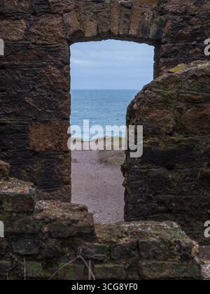Vue de la fenêtre en pierre accidentée encadrant l'océan, la plage et le ciel, créant un contraste frappant, Peterhead, Écosse, Royaume-Uni. Banque D'Images