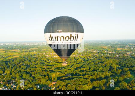 Sint-Martens-Latem, Belgique - 25 août 2025 : vue aérienne d'une montgolfière survolant une forêt dense et verdoyante, un contraste saisissant avec le ciel dégagé. Banque D'Images