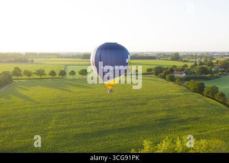 Sint-Martens-Latem, Belgique - 09 septembre 2023 : vue aérienne d'une montgolfière dérive sereinement au-dessus de champs verdoyants, un patchwork de nature peint sous la lumière douce et diffuse du soleil. Banque D'Images