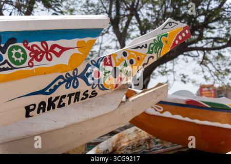 Dakar, Sénégal - 12 mai 2025 : vue de prouches colorées de bateaux de pêche amarrés à la plage de Soumbédioune, une exposition vibrante de l'art local contre le rivage sablonneux. Banque D'Images