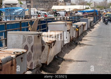 Dakar, Sénégal - 12 mai 2025 : vue de boîtes métalliques altérées bordant le pont de la plage de Soumbédioune, leurs motifs délavés contrastant avec l'animation de la ville en toile de fond. Banque D'Images