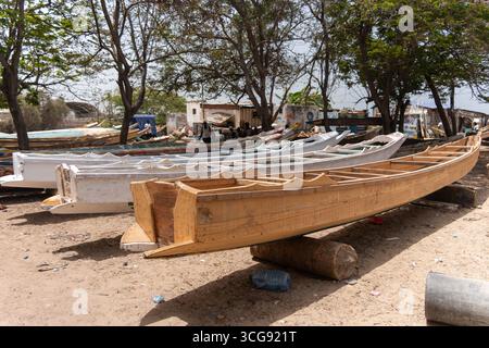 Dakar, Sénégal - 12 mai 2025 : vue de bateaux en bois reposant sur le sol sablonneux de la plage de Soumbédioune, à l'ombre des arbres, mettant en valeur l'artisanat et la culture maritime. Banque D'Images