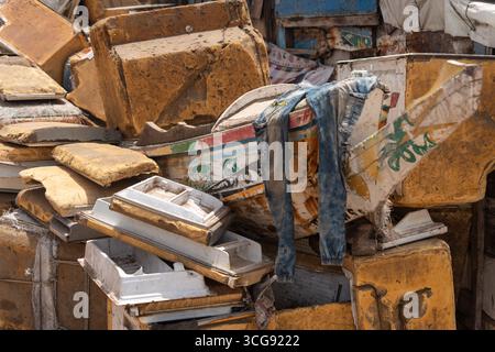 Dakar, Sénégal - 12 mai 2025 : vue de débris et d'ordures jetés, avec une paire de jeans bleus drapés parmi les formes texturées et altérées à la plage de Soumbédioune. Banque D'Images