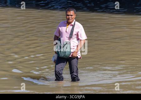 SAMUT PRAKAN, THAÏLANDE, 19 nov 2024, Un homme patente dans une rue inondée Banque D'Images