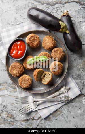 entrée d'aubergines frites boules d'aubergines végétariennes avec sauce tomate et épices gros plan dans l'assiette sur la table. Vue de dessus verticale Banque D'Images