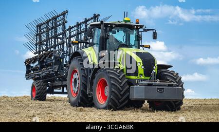 Tracteur agricole moderne sur chaume fauché dans le champ en automne sous ciel bleu. Culture du sol avant semis de plantes, cultures agricoles, rural na Banque D'Images