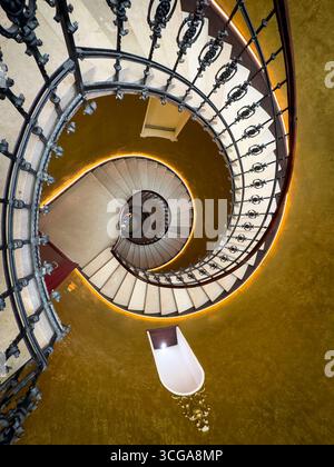 Élégant escalier en colimaçon entouré de murs texturés dorés avec balustrade en fer ornée vue d'en haut. Banque D'Images