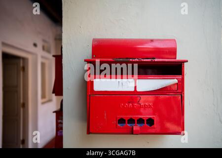 Une boîte aux lettres rouge est montée sur un mur, avec du courrier visible à l'intérieur et de la peinture légèrement usée sur le couvercle supérieur. Banque D'Images