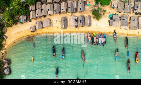 Une vue aérienne imprenable sur un village balnéaire tropical avec des rangées de petites cabanes le long du littoral, les bateaux de pêche traditionnels sont ancrés dans le turquois Banque D'Images