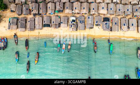 Une vue aérienne imprenable sur un village balnéaire tropical avec des rangées de petites cabanes le long du littoral, les bateaux de pêche traditionnels sont ancrés dans le turquois Banque D'Images