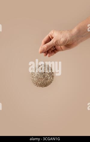 Boule brillante de Noël dans la main de femme sur fond beige. Carte de voeux de Noël. Concept du nouvel an. Mousse moka. Format vertical. Banque D'Images