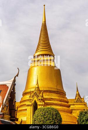 Une vue rapprochée d'un stupa doré avec une flèche pointue, entouré d'une végétation luxuriante et d'une architecture traditionnelle Banque D'Images