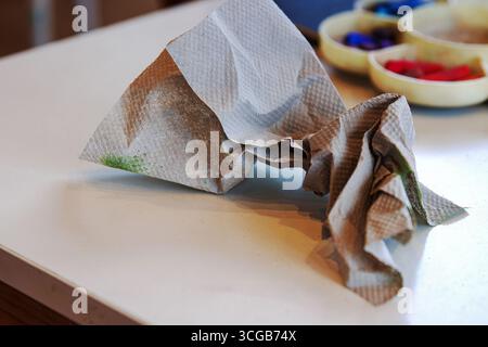 Gros plan d'une serviette en papier froissée avec des taches de craie pastel colorées reposant sur une table blanche Banque D'Images