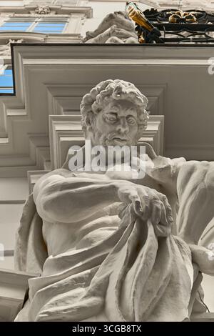 Gros plan détaillé d'une sculpture classique représentant un homme barbu aux cheveux bouclés, partiellement drapé et intégré dans l'architecture du bâtiment. Banque D'Images