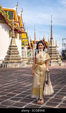 Une femme en tenue traditionnelle thaïlandaise se tient devant des pagodes ornées et des toits de temple colorés Banque D'Images