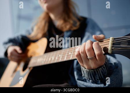 Jeune femme caucasienne adulte pratiquant des accords sur guitare acoustique à l'extérieur Banque D'Images