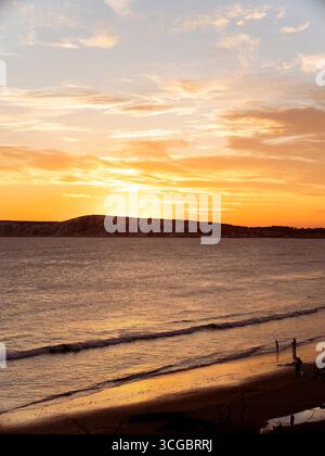 Les gens nagent dans la mer à la plage de Compton Bay sur l'île de Wight pendant un coucher de soleil à la fin de l'été. Banque D'Images