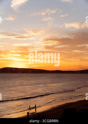 Les gens nagent dans la mer à la plage de Compton Bay sur l'île de Wight pendant un coucher de soleil à la fin de l'été. Banque D'Images
