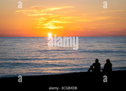 Couple assis sur la plage regardant le coucher du soleil sur le golfe d'Amérique, anciennement le golfe du Mexique, de Vencie Beach à Vencie Florida USA Banque D'Images