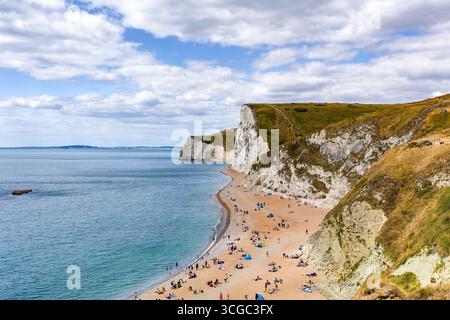 Foules de personnes se relaxant sur une plage de sable fin sous les falaises de craie blanche, côte jurassique Banque D'Images