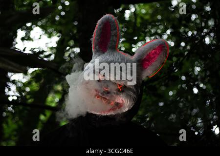 Masque de lapin LED blanc effrayant avec des lumières rouges incandescentes et de la fumée s'élevant des yeux et de la bouche dans la forêt sombre Banque D'Images