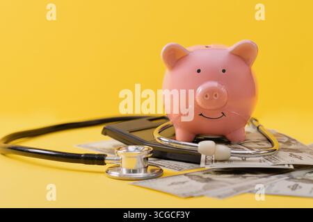 Tirelire rose sur la calculatrice avec des billets de dollar dispersés et stéthoscope sur fond jaune. Banque D'Images