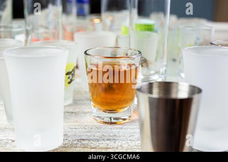 Une vue de plusieurs verres à dose vides sur une surface de table en bois, avec un verre à dose unique au milieu avec de l'alcool à l'intérieur. Banque D'Images