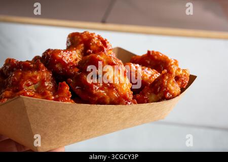Une vue d'une main tenant un plateau d'ailes de poulet glacées asiatiques. Banque D'Images