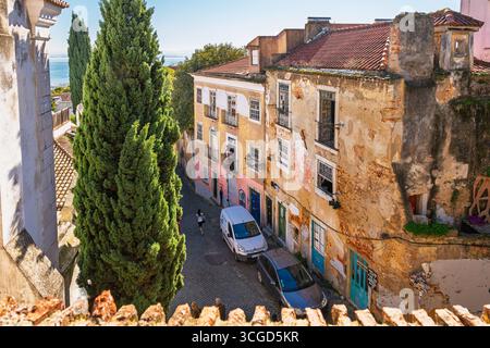 Un musicien se tient sur un balcon et sérénade les passants dans la rue pavée ci-dessous dans le quartier médiéval vallonné de l'Alfama à Lisbonne, au Portugal. Banque D'Images