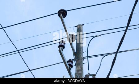 Vue rapprochée de plusieurs lignes électriques reliées à un poteau de service avec isolants, placées contre un ciel bleu vif. Banque D'Images