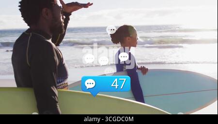 Debout sur le rivage sablonneux, deux surfeurs ombrageant les yeux et accrochant les planches de surf, portant des combinaisons de plongée Banque D'Images