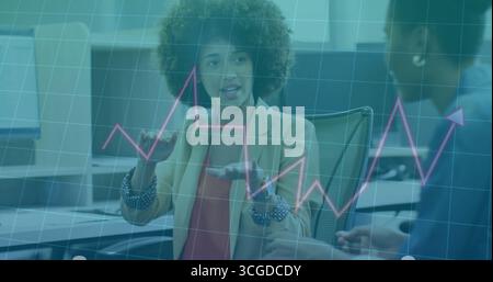 Femme gestuelle en blazer beige et chemisier rouge analysant les données, avec graphique linéaire superposé dans le bureau Banque D'Images