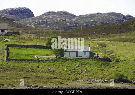 Chalet en pierre isolé sur une colline verte avec des murs de pierre et des montagnes en arrière-plan, Highlands, Kinlochbervie, Écosse, Royaume-Uni Banque D'Images