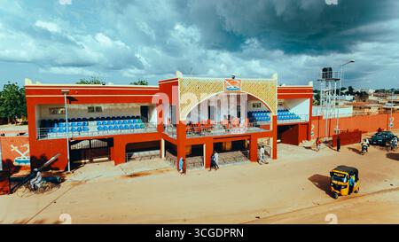Vue aérienne du bâtiment rouge vif contrastant avec le premier plan sablonneux et le ciel nuageux, debout bien en vue au cœur de la ville, Daura, Katsina, Nigeria. Banque D'Images