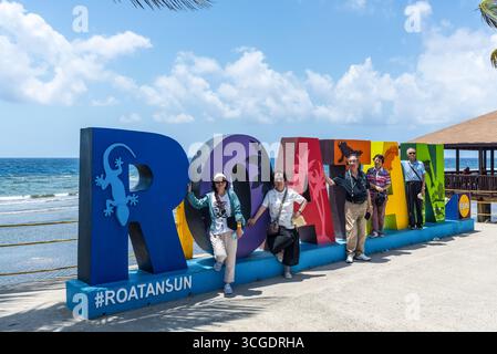 Isla de Roatan, Honduras - 16 avril 2024 : les touristes prennent des photos devant le panneau coloré de Roatan sur l'île de Roatan, Honduras. Banque D'Images