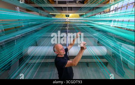 PRODUCTION - 26 août 2025, Saxe, Chemnitz : le maître tisserand Mario Thümer travaille sur une machine à tisser pour tapis de glisse textiles dans l'usine de production de Mr. Snow à Chemnitz. Environ 13 000 fils se réunissent ici et sont tissés en boucles flexibles. La structure offre une bonne surface de contact pour les carres des skis. La société basée à Chemnitz dessert désormais tout le spectre du ski, du ski de fond classique aux pistes freestyle. Dimanche (31.08.2025), la dernière installation avec de la neige textile de Chemnitz ouvrira au Danemark, une arène de ski de 5 000 mètres carrés à 360 degrés avec six diffe Banque D'Images