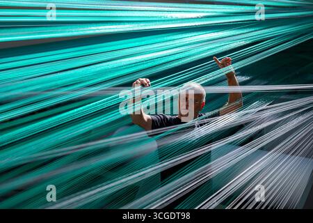 PRODUCTION - 26 août 2025, Saxe, Chemnitz : le maître tisserand Mario Thümer travaille sur une machine à tisser pour tapis de glisse textiles dans l'usine de production de Mr. Snow à Chemnitz. Environ 13 000 fils se réunissent ici et sont tissés en boucles flexibles. La structure offre une bonne surface de contact pour les carres des skis. La société basée à Chemnitz dessert désormais tout le spectre du ski, du ski de fond classique aux pistes freestyle. Dimanche (31.08.2025), la dernière installation avec de la neige textile de Chemnitz ouvrira au Danemark, une arène de ski de 5 000 mètres carrés à 360 degrés avec six diffe Banque D'Images