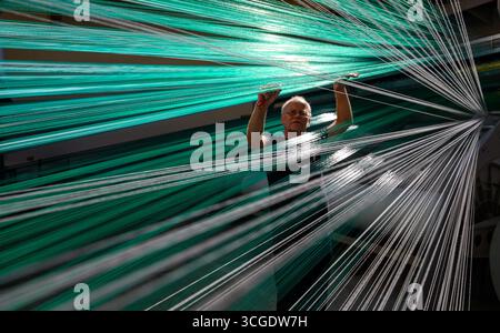 PRODUCTION - 26 août 2025, Saxe, Chemnitz : le maître tisserand Mario Thümer travaille sur une machine à tisser pour tapis de glisse textiles dans l'usine de production de Mr. Snow à Chemnitz. Environ 13 000 fils se réunissent ici et sont tissés en boucles flexibles. La structure offre une bonne surface de contact pour les carres des skis. La société basée à Chemnitz dessert désormais tout le spectre du ski, du ski de fond classique aux pistes freestyle. Dimanche (31.08.2025), la dernière installation avec de la neige textile de Chemnitz ouvrira au Danemark, une arène de ski de 5 000 mètres carrés à 360 degrés avec Banque D'Images