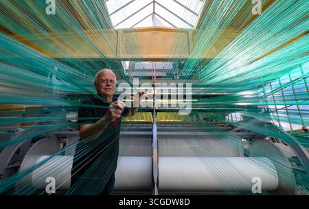 PRODUCTION - 26 août 2025, Saxe, Chemnitz : le maître tisserand Mario Thümer travaille sur une machine à tisser pour tapis de glisse textiles dans l'usine de production de Mr. Snow à Chemnitz. Environ 13 000 fils se réunissent ici et sont tissés en boucles flexibles. La structure offre une bonne surface de contact pour les carres des skis. La société basée à Chemnitz dessert désormais tout le spectre du ski, du ski de fond classique aux pistes freestyle. Dimanche (31.08.2025), la dernière installation avec de la neige textile de Chemnitz ouvrira au Danemark, une arène de ski de 5 000 mètres carrés à 360 degrés avec six diffe Banque D'Images