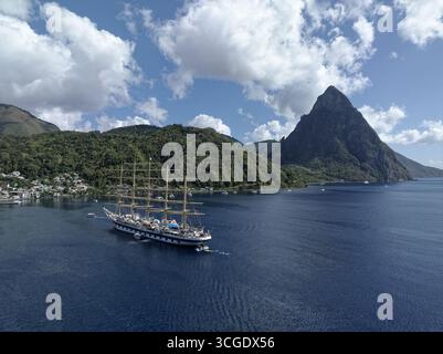Vue aérienne d'un majestueux voilier traversant les eaux bleues profondes près de collines verdoyantes et des emblématiques Pitons, Soufrière, Sainte-Lucie. Banque D'Images