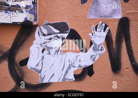 Un garçon dans une veste de protection, portant des lunettes de réalité virtuelle, regardant l'espace. Street art, graffiti à Bologne, Italie. Banque D'Images