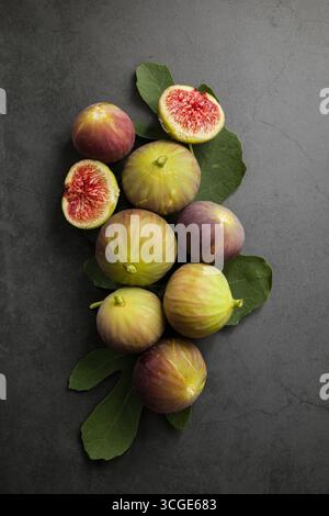 Figues fraîches placées sur le dessus des feuilles vertes sur la table noire. Banque D'Images