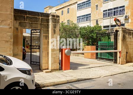 Checkpoint avec portes de sécurité métalliques automatiques, une barrière moderne et un miroir mural rond, installé contre un bâtiment en pierre avec fenêtres et verdure Banque D'Images