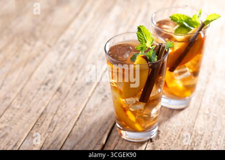 Rafraîchissant thé glacé à la pêche dans un verre avec des glaçons et de la cannelle sur une table en bois Banque D'Images