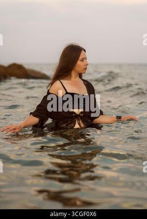 Une jeune femme mignonne dans la mer. Elle est debout dans l'eau, au coucher du soleil Banque D'Images