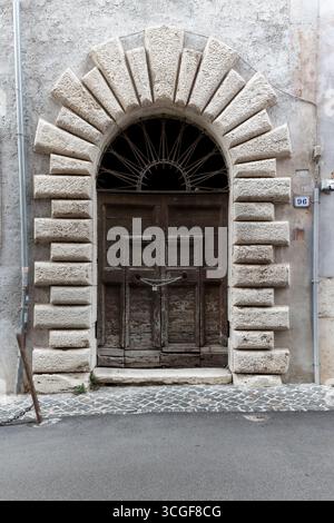 Vieille porte voûtée en bois avec cadre en pierre rustique dans un bâtiment historique, Tivoli, Lazio, Italie. Détail architectural. Banque D'Images